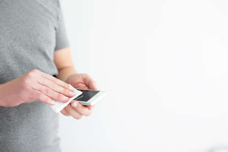 coronavirus protection and disinfection concept - man disinfecting smart phone screen with alcohol...
