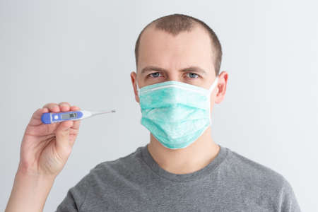 health care, illness and pandemic concept - sick man in protective mask showing thermometer with...