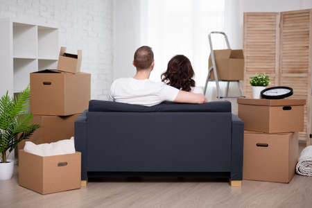 back view of happy young couple in new house and stack of cardboard boxes after moving day