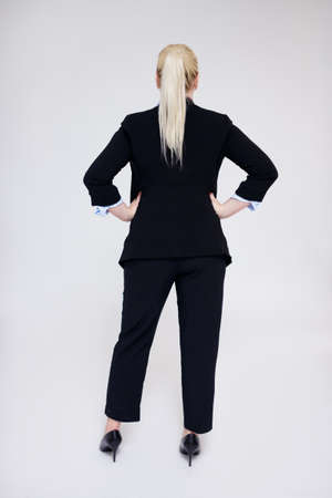 full length back view of plus size blonde woman in black business suit posing over gray background