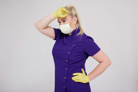 portrait of tired or overworked female nurse, beautician, cosmetologist or other beauty industry worker in uniform and mask posing over gray backgroundの写真素材