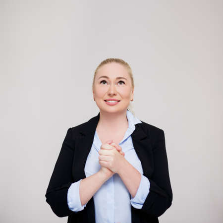 hope, faith and business concept - portrait of beautiful happy blonde woman praying and looking up over gray background with copy spaceの写真素材