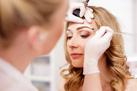 make up and beauty concept - close up of make up artist painting eyebrows at beauty studioの写真素材