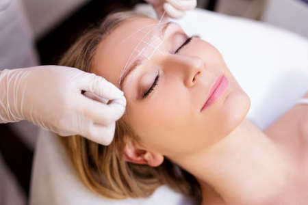 close up portrait of young woman undergoing eyebrow correction procedure in beauty salon