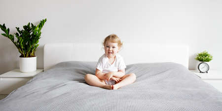 happy cute little girl sitting on bed in modern bedroomの写真素材