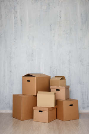 moving day concept  - brown cardboard boxes with belongings stacked on the floor and copy space over gray wall backgroundの写真素材