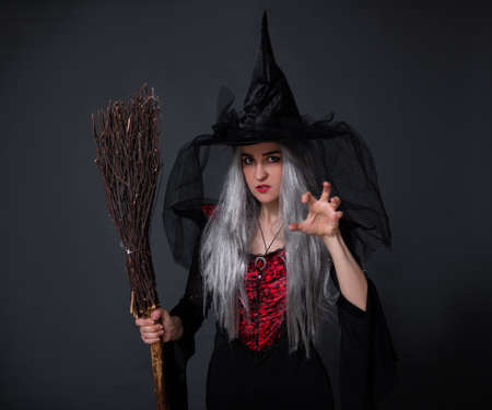 portrait of mysterious woman in black witch halloween costume posing with broom over black backgroundの写真素材