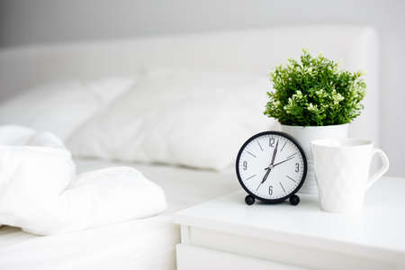 good morning concept - alarm clock and cup of coffee on bedside table and unmade bed at home or hotelの写真素材