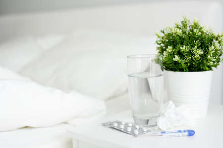 health care and illness concept - close up of glass of water, pills and thermometer on bedside tableの写真素材