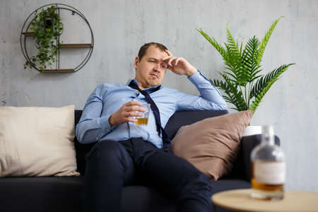 alcoholism, business and stress concept - drunk businessman drinking alcohol at home or office