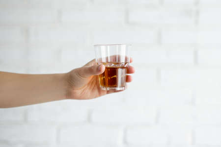 close up of whiskey glass in male hand over white brick wall  backgroundの写真素材