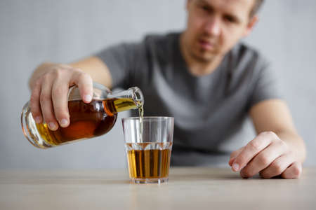 alcoholism concept - close up of male hands pouring alcohol into glassの写真素材