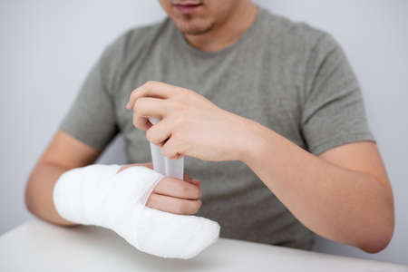fracture and first aid concept - close up of young man bandaging his handの写真素材