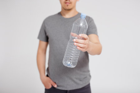 recycling and waste sorting concept - plastic bottle in male hands over grey background with copy spaceの写真素材