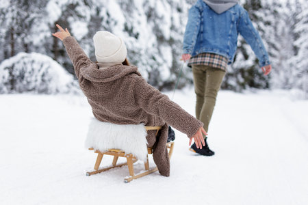 back view of  man pulling sledge with woman in winter forest