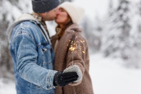 young couple with sparklers kissing in winter forest or parkの写真素材