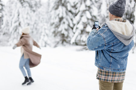 man photographing his girlfriend in winter forestの写真素材