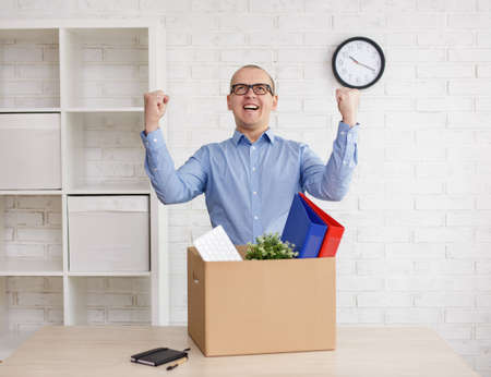 first or last day in office - happy man with his belongings in cardboard boxの写真素材
