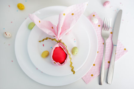 happy easter concept - top view of easter egg wrapped in pink napkin shaped like bunny ears