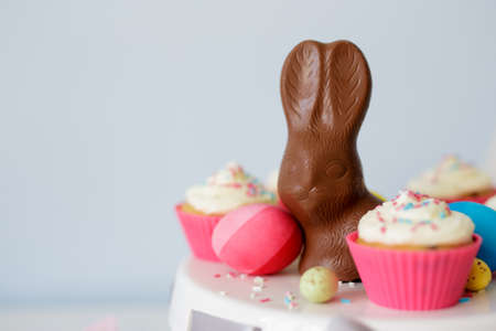 Easter sweets and decorations - cupcakes, painted eggs and chocolate bunny and copy space over blue...