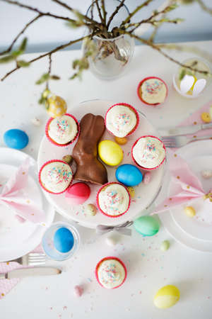 spring, holidays and easter concept - top view of decorated table with pussy willow branch, cupcakes, colorful painted eggs and bunniesの写真素材