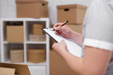 work and business concept - close up of male hands writing something in clipboard in warehouse