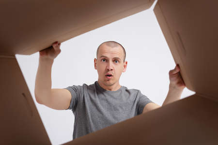 astonished man  unpacking and opening a carton gift box and looking inside. View from the box