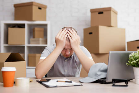 work, business, bankruptcy and depression concept - sad or tired postman in post office with boxes...