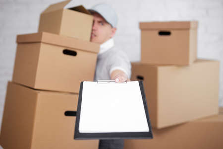 postal delivery or moving day concept - tired man with many boxes giving a clipboard to signの写真素材