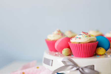 Easter sweets and decorations - close up of cream cupcakes and colorful painted eggs over white wall...