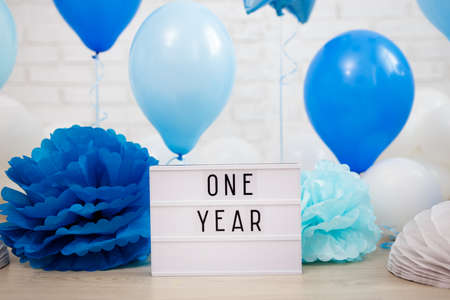 baby boy first birthday party decoration - blue air balloons, paper balls and lightbox with one year text over white brick wallの写真素材