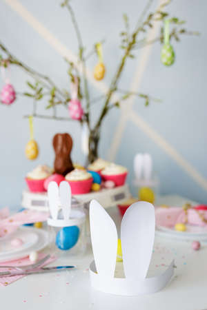 Happy Easter concept - close up of paper bunny ears on decorated table with cupcakes and colorful painted Easter eggsの写真素材