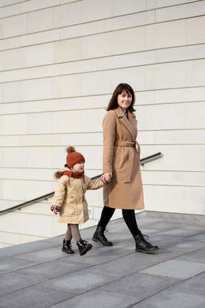 family, motherhood, love and care concept - happy mother and her little daughter walking hand in...