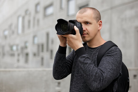 portrait of male photographer taking photo with modern dslr camera over concrete building background