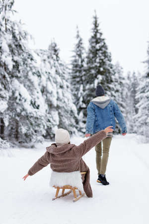back view of  man pulling sledge with his girlfriend in winter forest or parkの写真素材