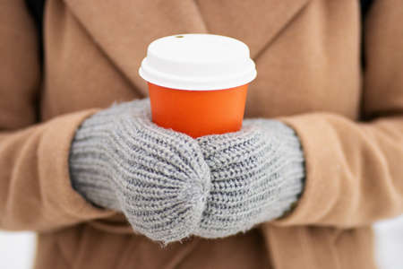 Close up of hands in mittens with cup of hot coffee