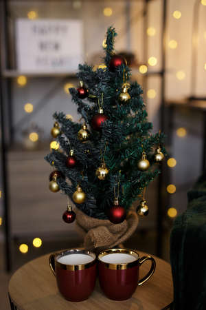 decorated small christmas tree with two cups of coffee over led lights background