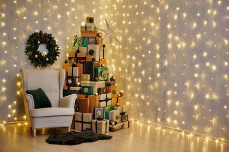 Decorated living room with armchair, wreath and Christmas gift boxes laid out in the shape of a...