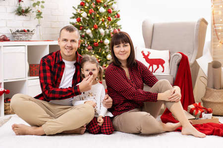 Funny family in pajamas sitting on carpet in christmas decorated roomの写真素材