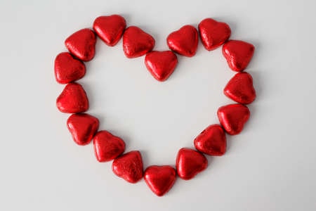 chocolate sweets hearts in red foil in the shape of a heart over white backgroundの写真素材