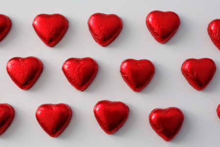 Love and Valentine's day background - close up of heart shape chocolate candies in red foil over white backgroundの写真素材