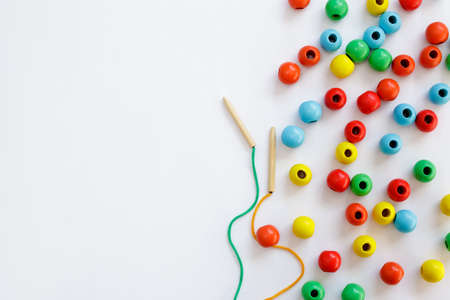 Children development, coordination and cognitive skills concept - toy for motor skills development - colorful wooden beads, lace and needle over white background with copy spaceの写真素材