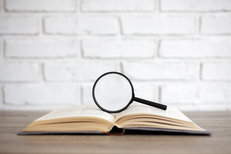reading, education and research concept - open old book with magnifying glass on the table, copy...
