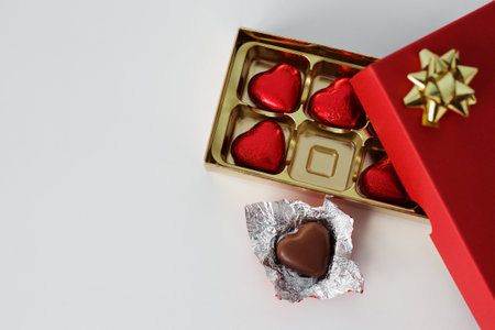 close up of gift box of heart shape chocolate candies in red foil and copy space over white...
