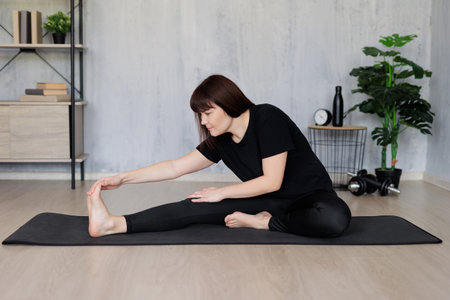 sport and healthy lifestyle concept - young woman doing stretching exercises sitting on yoga mat in living room at homeの写真素材