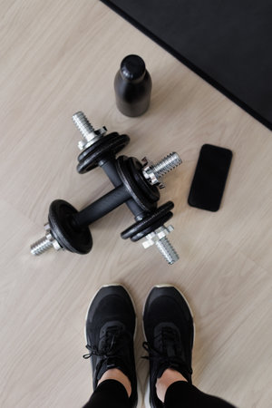 sport and fitness background - top view of female legs in black sneakers, dumbbells, bottle of water, yoga mat and smartphoneの写真素材