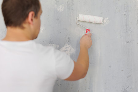 Back view of painter painting grey wall with paint rollerの写真素材