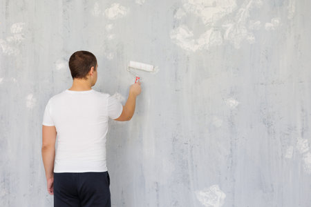 rear view of painter man painting the wall with paint roller, copy space over grey wallの写真素材