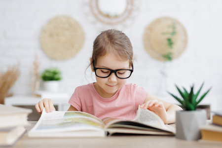childhood and education concept - cute little schoolgirl reading book at homeの写真素材