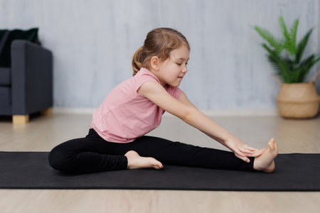 portrait of cute little girl doing stretching exercises on yoga mat at homeの写真素材